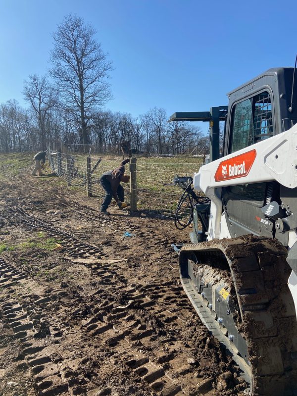 A skid steer installing wire fencing on a farm