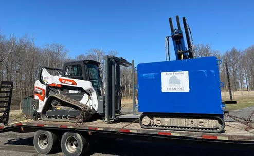 A truck trailer loaded with a skid steer and fencing equipment